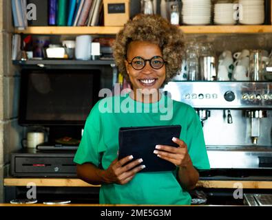 Portrait d'une jeune femme afro-américaine avec une tablette regardant l'appareil photo dans un pub. Femme entrepreneuriale, petite entreprise Banque D'Images