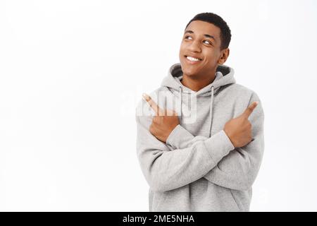 Portrait d'un homme souriant et rêveur pointant les doigts latéralement, en choisissant, ayant une variété de choix, debout sur fond blanc Banque D'Images
