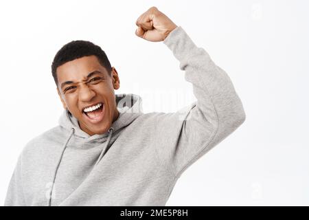 Gagnant. Homme afro-américain enthousiaste qui célèbre, élève le poing, proteste, atteint son but et triomphant, se tenant sur fond blanc Banque D'Images