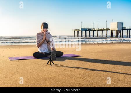 Femme mince instructeur de yoga donnant la formation de yoga en ligne dans un appareil photo de téléphone mobile. Yoga et méditation pour le réseau social. Banque D'Images