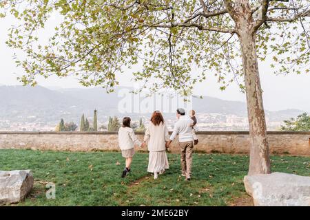 Une jeune famille avec deux enfants, une adolescente et un petit garçon, marche main dans la main sur fond des collines verdoyantes et des vignobles de l'Italie Banque D'Images