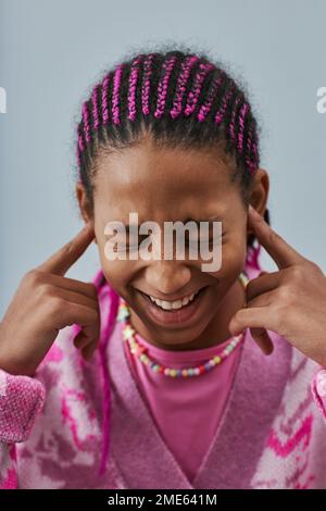 Portrait en gros plan d'une adolescente noire expressive portant des oreilles roses et des oreilles de fermeture sur fond bleu Banque D'Images