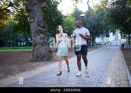 Couple sur la date dans le parc, la crème glacée et de tenir les mains à l'extérieur, l'amour et l'engagement dans la relation. Romance dans la nature, l'homme noir et la femme mangent le dessert Banque D'Images