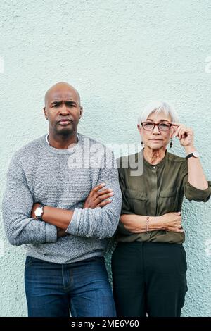 Nous prenons notre entreprise au sérieux. Portrait de deux hommes d'affaires matures se posant ensemble contre un mur à l'extérieur. Banque D'Images