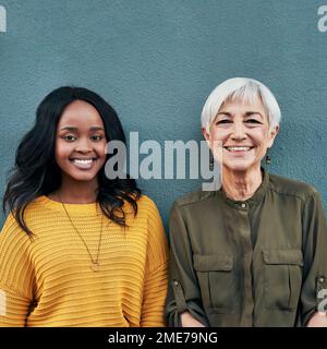 Apprendre des meilleurs chaque jour. Portrait d'une jeune femme d'affaires gaie et mûre se posant ensemble contre un mur à l'extérieur. Banque D'Images