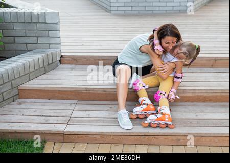 Une petite fille en patins à roulettes et sa mère s'assoient sur une échelle en bois et embrasse à l'extérieur. Banque D'Images