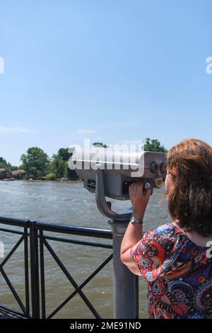 Femme latine mature regardant à travers des jumelles publiques sur la rive de la rivière Lujan à Tigre, Buenos Aires, Argentine. Banque D'Images