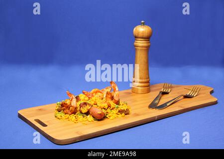 Riz traditionnel paella de Valence Espagne, fait avec des coquillages safran, des crevettes et des légumes servis sur une planche de bois et une main prenant une fourchette Banque D'Images