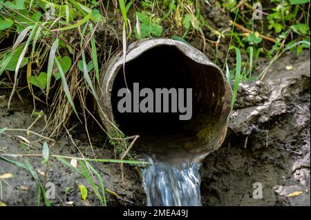 Eau s'écoulant de la sortie ouverte d'un carreau de drainage agricole métallique Banque D'Images