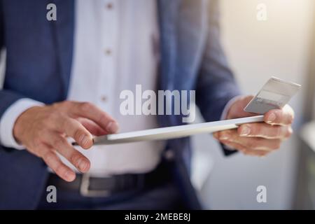 Pas de atm, Pas de problème. un homme d'affaires méconnaissable utilisant une tablette numérique et une carte de crédit dans un bureau moderne. Banque D'Images