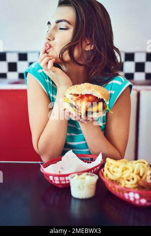 C'est un hamburger savoureux. une jeune femme attrayante qui apprécie un hamburger dans un restaurant rétro. Banque D'Images