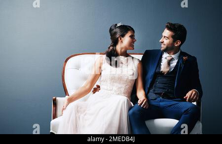 C'était une expérience folle. Photo studio d'un jeune couple récemment marié assis ensemble sur un canapé sur fond gris. Banque D'Images