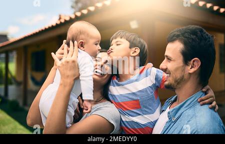 Il voulait toujours un petit frère. une jeune famille heureuse de quatre à l'extérieur avec leur maison en arrière-plan. Banque D'Images