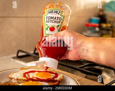 Londres. ROYAUME-UNI- 01.22.2023. Une personne pressant une bouteille de ketchup de tomate Heinz sur des œufs frits sur du pain grillé. Banque D'Images