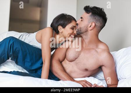 Le premier baiser de la journée. un jeune couple affectueux et marié au lit à la maison. Banque D'Images