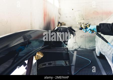 Personne non reconnaissable portant des gants bleus peignant le corps de la voiture noir à l'aide d'un aérographe. Peinture automobile. Prise de vue horizontale en intérieur. Photo de haute qualité Banque D'Images