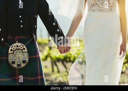 Nous sommes liés ensemble. une mariée et un marié méconnaissables tenant les mains et marchant ensemble à l'extérieur pendant la journée. Banque D'Images