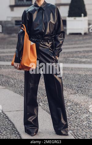 Milan, Italie - 24 février 2022: Femme en cuir noir combinaison debout avec main dans la poche et sac orange. Banque D'Images