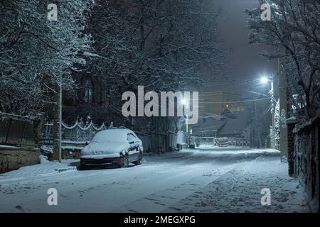 Voiture dans une rue enneigée dans une petite ville la nuit. Banque D'Images