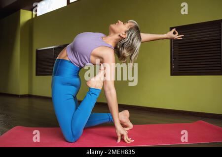 Une femme menant un mode de vie sain et pratiquant le yoga, exécute une variation de l'exercice Ushtrasana, pose de chameau, s'exerçant seul dans sportswear o Banque D'Images