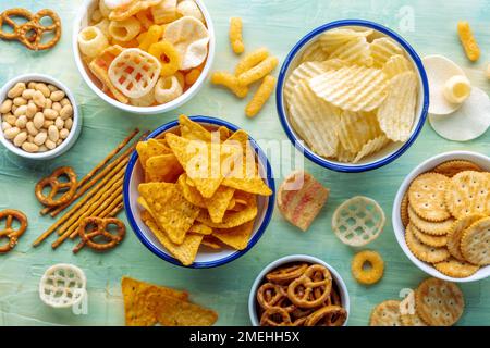 Collations salées. Repas de fête sur fond bleu. Chips de pommes de terre et de tortilla, craquelins et autres hors-d'œuvre dans des bols, grenaille à plat au-dessus Banque D'Images