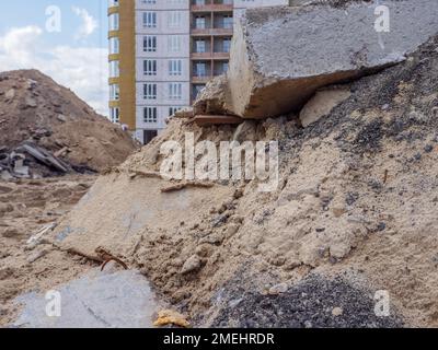 Un chantier de construction avec des piles de sable et un énorme bloc de béton au premier plan et un nouveau bâtiment en hauteur en arrière-plan à Kiev. Nouveau concept de district. Banque D'Images