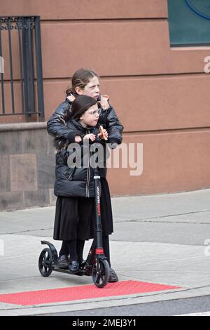 Les filles juives orthodoxes, probablement sœurs, arrêtent leur scooter à un coin en attendant que la lumière change. À Brooklyn, New York. Banque D'Images