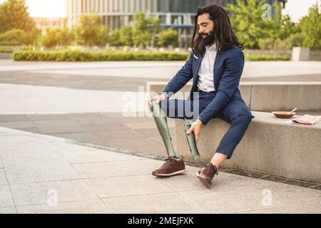 Homme d'affaires ajustant sa jambe prothétique à l'extérieur de l'immeuble de bureau - Focus sur la main droite Banque D'Images