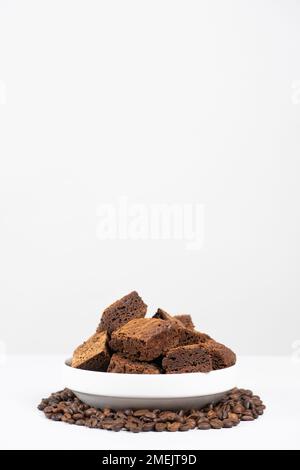 Gâteau au chocolat coupé en carrés dans une assiette blanche, brownie et grains de café, espace pour le texte Banque D'Images