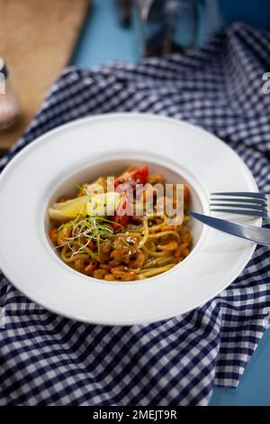 Spaghetti aux crevettes, citron et micro-vert. Déjeuner dans un plat blanc profond, gros plan. Pâtes avec fruits de mer, tomates et salade. Banque D'Images