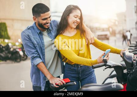 Jeune couple louant un vélo électrique avec une application pour smartphone - attention douce sur le visage de l'homme Banque D'Images