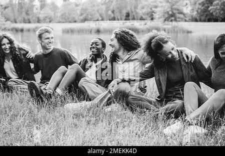 Amis multiethniques s'amusant assis sur l'herbe en plein air - Focus sur le visage de fille africaine droite - montage noir et blanc Banque D'Images