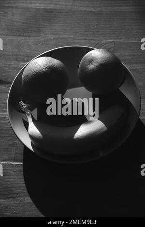 Visage souriant et heureux fait de fruits sur une assiette sur une ancienne table en bois. Alimentation saine, régime végétarien, concepts de pensée positive. Photographie en noir et blanc. Banque D'Images