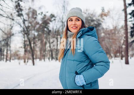 Portrait d'une jeune femme marchant dans un parc hivernal enneigé portant une veste de duvet bleue. Vêtements chauds pour le froid glacial Banque D'Images