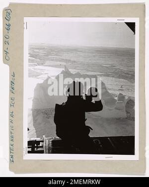 Silhouette d'un guardsman de la côte teinte aérienne 'bombarder' un Iceberg. Membre d'équipage à genoux, silhoueté dans la porte de chargement arrière d'un U.S. L'avion de patrouille sur glace HC-130-B de la Garde côtière, vise soigneusement une bombe à colorant B chlorure de calcium-rhodamine à l'iceberg ci-dessous, située dans un champ de glace du détroit de Davis au large de l'île de Baffin. Incrusté d'une coloration vermillion brillante, l'iceberg est marqué pour une identification future et un suivi aérien. Cette méthode de marquage des icebergs, mise au point par l'unité océanographique de la Garde côtière à Washington, D.C., a été utilisée pour la première fois dans la patrouille des glaces de 1966 sur les cibles des icebergs situées Banque D'Images