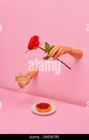 Photographie d'art pop. Main féminine de papier rose avec champagne et fleur de rose sur une délicieuse tarte aux baies Banque D'Images