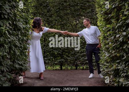 Les jeunes mariés tiennent les mains et se regardent les uns les autres dans l'amour. Jeunes mariés dans le parc d'été au milieu du feuillage. De jeunes amoureux heureux Banque D'Images