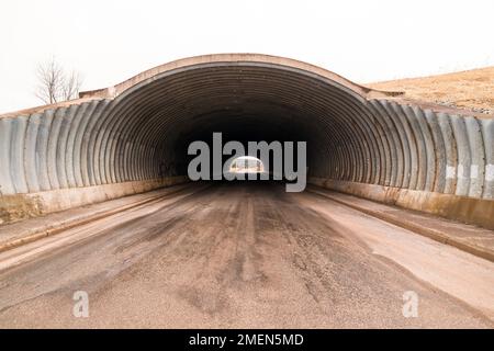 Long tunnel pour voitures et camions. Le tunnel est de forme demi-ovale et en métal nervuré. Le tunnel est droit, l'autre extrémité est visible. Ciel couvert au-dessus. Banque D'Images