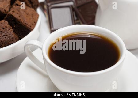 Café en gros plan dans une tasse, gâteau au chocolat et morceaux de chocolat sur fond blanc Banque D'Images