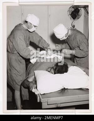 Les doigts de Mercy. À bord d'un LST habité par la Garde côtière pendant l'invasion de Cape Gloucester, en Nouvelle-Bretagne, un médecin de la Marine et un pharmacien de la Garde côtière effectuent une opération d'urgence sur un homme blessé. Un hôpital d'urgence a été installé dans la salle de garde de l'officier du navire. La Garde côtière et la Marine ont participé à l'invasion. Banque D'Images