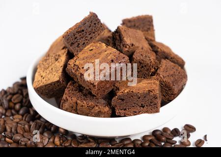 Gâteau au chocolat coupé en carrés dans une assiette blanche, brownie et grains de café. Banque D'Images