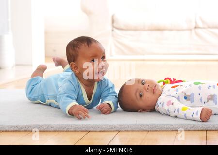 Deux bébés garçons couchés à l'avant et à l'arrière sur un tapis, 4 mois Banque D'Images