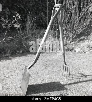 1950s, historique, équilibre de vie..., à l'extérieur sur une pelouse, une bêche de jardin à manche en bois et une fourche de jardin équilibrée les unes par rapport aux autres. Banque D'Images