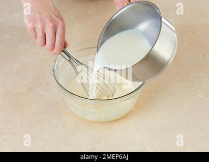 Verser le lait chaud dans le mélange d'œufs, tout en chuchotant, pour faire de la crème patissière pour la tarte Banque D'Images