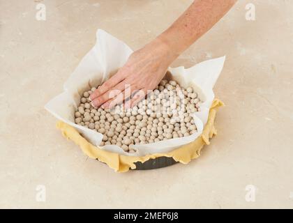 Préparer un tarte au custard, en recouvrant le présentoir à pâtisseries de papier sulfurisé et en le pesant avec des haricots Banque D'Images