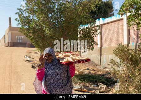 ASSOUAN, ÉGYPTE - 29 décembre 2022. Jeune femme nubienne, arabe, musulmane avec voile et vêtements traditionnels avec pain pita frais fait main chaque jour scène Banque D'Images