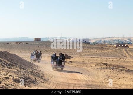 ASSOUAN, ÉGYPTE - 29 décembre 2022. Touristes assis dans le vieux transport traditionnel en Egypte dans le sable aride paysage Banque D'Images