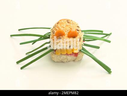 Un rouleau de pain fait pour ressembler à un monstre avec des carottes pour les yeux, du maïs sucré pour les dents et de la ciboulette pour les jambes. Banque D'Images