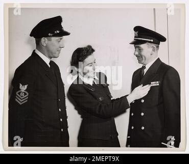 Spar admire les médailles des héros. Mlle Marjorie G. Taylor, 25 ans, de Washington, D.C., futur officier de la Garde côtière, ADMIRE avec sourire les rubans de service portés par l'Adjudant Machiniste James D. Fox (à droite) de la Garde côtière, qui a subi 112 attaques aériennes et 30 pillages au cours de ses 90 jours sur Guadalcanal. Le chef Boatswain's Mate Hunter Wood (à gauche), 34 ans, illustrateur commercial, qui a rejoint la Garde côtière immédiatement après l'attaque de Pearl Harbor, a assisté au récent naufrage du porte-avions britannique Avenger, et a ensuite peint la scène vivante sur un morceau de navire Banque D'Images