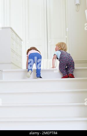 Garçon et fille grimpant les escaliers, 2 ans et 18 mois Banque D'Images